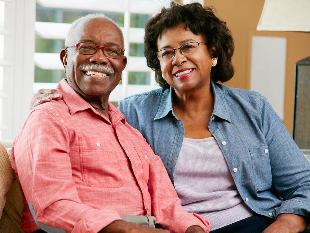 Couple sitting on couch and smiling at the camera.