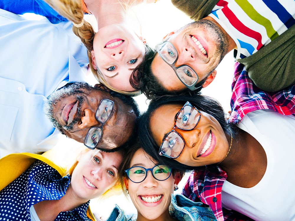 Teenagers in a circle looking down into the camera and smiling.