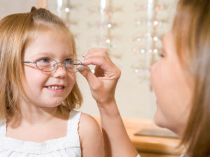 Woman putting glasses on a young girl at the eye doctor.