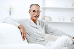 Mature man using sitting on the sofa at home and looking at the camera.