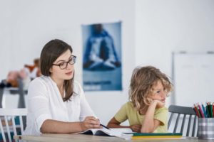 A bored child refusing to cooperate with his private teacher while doing homework.